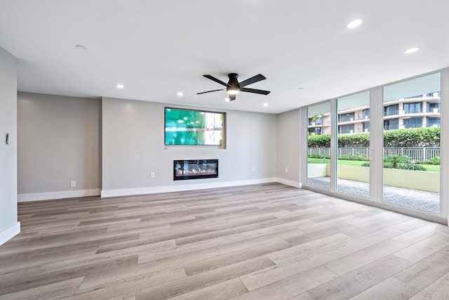 unfurnished living room featuring expansive windows, ceiling fan, and light wood-type flooring