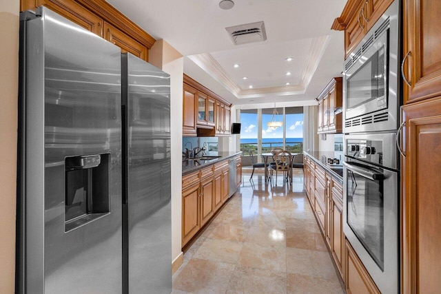 kitchen with appliances with stainless steel finishes, decorative light fixtures, sink, ornamental molding, and a raised ceiling