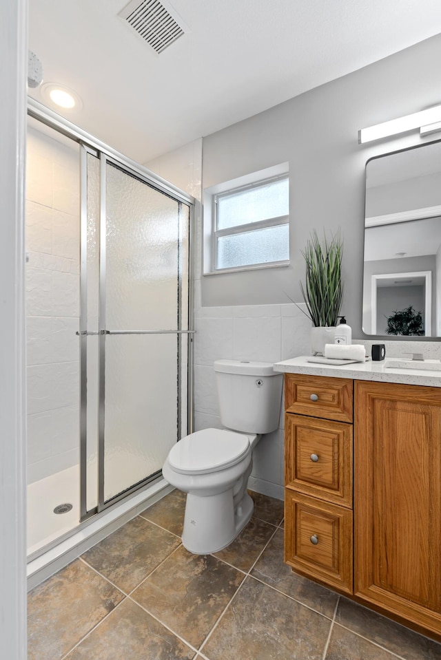 bathroom with vanity, toilet, an enclosed shower, and tile walls