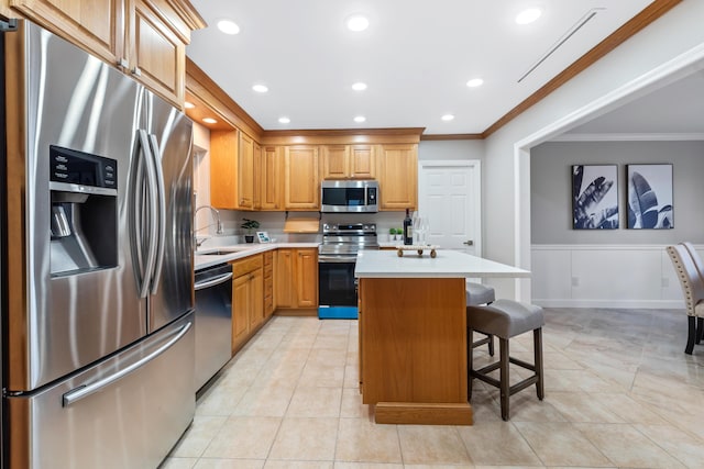 kitchen with a kitchen bar, sink, ornamental molding, appliances with stainless steel finishes, and a kitchen island