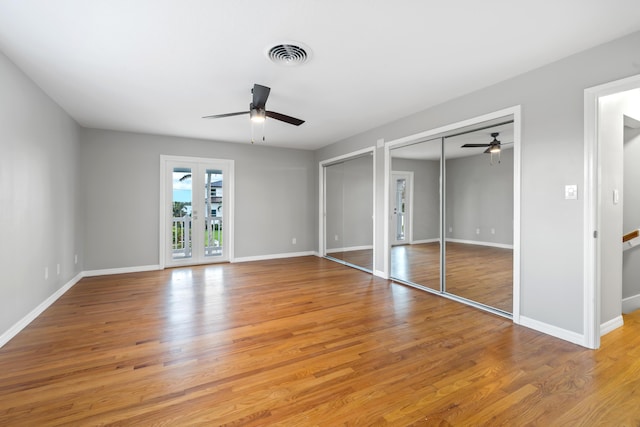 unfurnished bedroom with multiple closets, ceiling fan, light hardwood / wood-style floors, and french doors