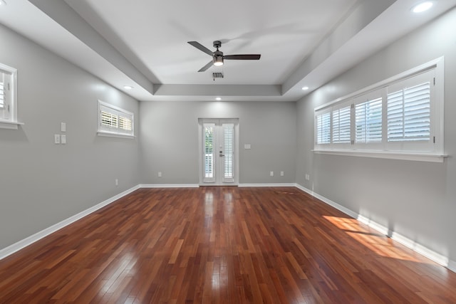 empty room with plenty of natural light, dark wood-type flooring, ceiling fan, and a tray ceiling