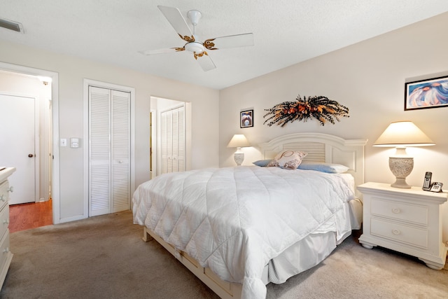 bedroom featuring ceiling fan, light carpet, and two closets