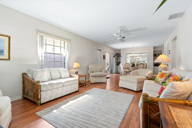 living room featuring hardwood / wood-style flooring, ceiling fan with notable chandelier, and a textured ceiling