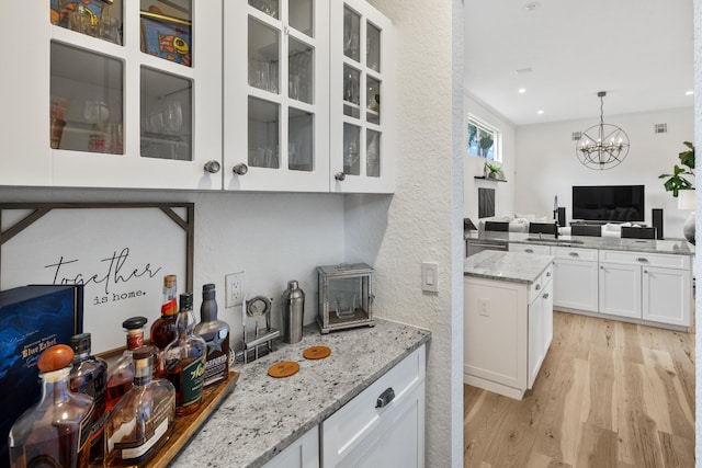 kitchen with decorative light fixtures, white cabinetry, light hardwood / wood-style floors, light stone countertops, and an inviting chandelier