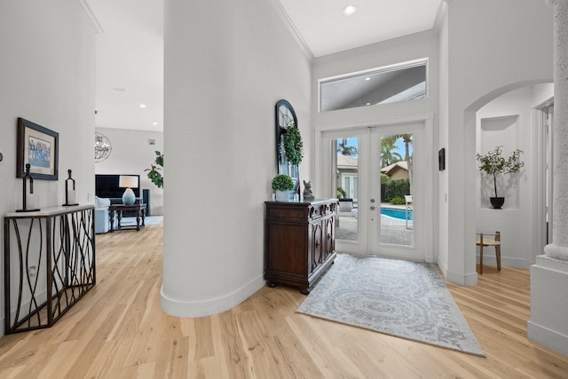 foyer entrance featuring crown molding, light hardwood / wood-style floors, french doors, and a high ceiling