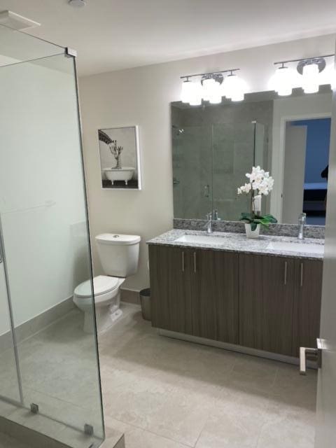 bathroom featuring tile patterned floors, vanity, toilet, and a shower with shower door