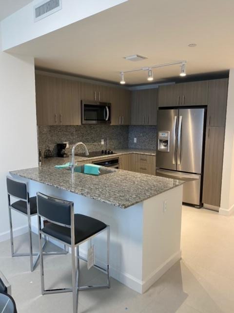 kitchen with appliances with stainless steel finishes, kitchen peninsula, light stone countertops, and backsplash