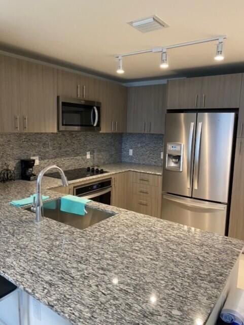 kitchen featuring sink, appliances with stainless steel finishes, backsplash, track lighting, and light stone countertops