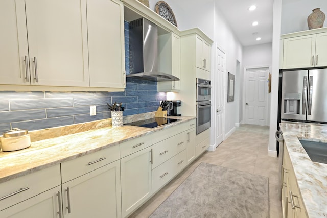 kitchen featuring light stone counters, wall chimney range hood, tasteful backsplash, and appliances with stainless steel finishes