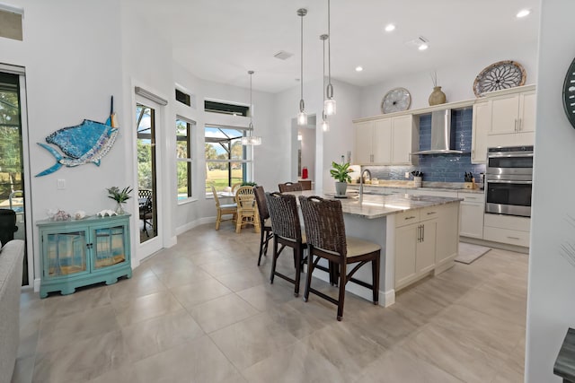 kitchen featuring sink, tasteful backsplash, an island with sink, stainless steel double oven, and wall chimney range hood