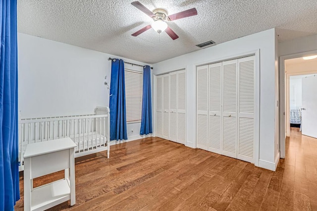 unfurnished bedroom with multiple closets, ceiling fan, wood-type flooring, and a textured ceiling