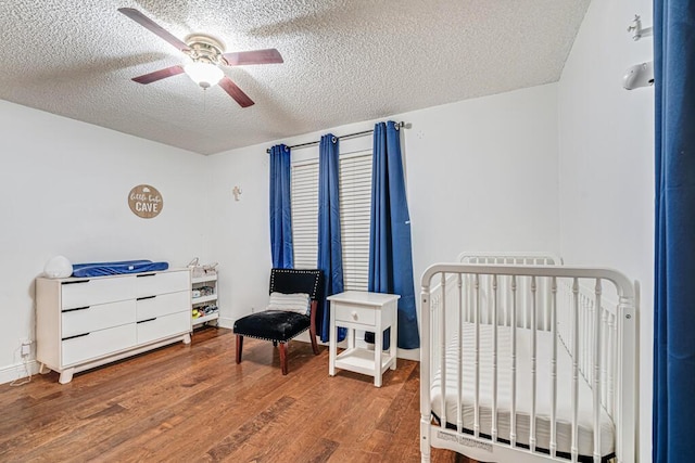 bedroom featuring ceiling fan, hardwood / wood-style floors, a textured ceiling, and a crib