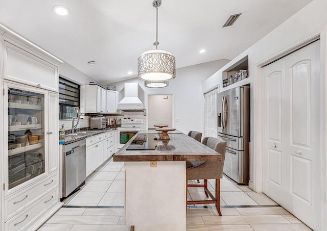 kitchen featuring premium range hood, a kitchen island, pendant lighting, stainless steel appliances, and white cabinets