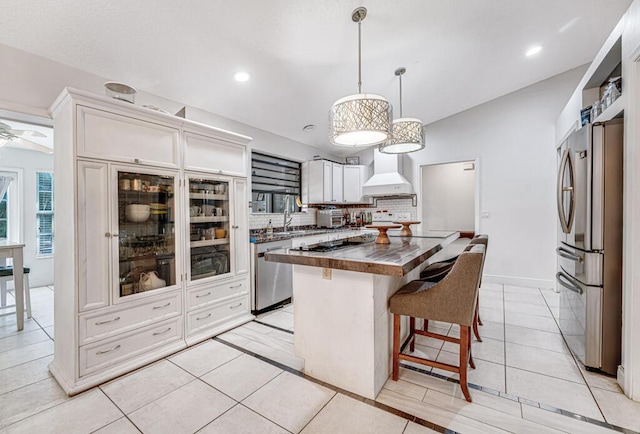 kitchen with pendant lighting, wooden counters, premium range hood, stainless steel appliances, and white cabinets