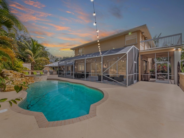 pool at dusk featuring a patio and glass enclosure