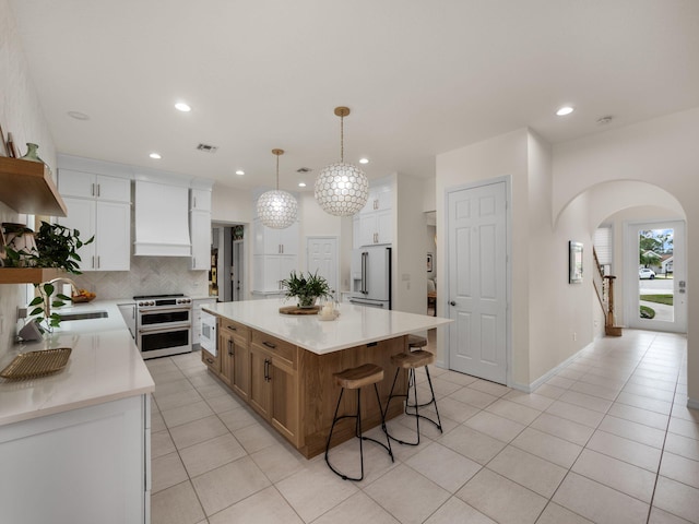 kitchen featuring a kitchen island, pendant lighting, high end refrigerator, white cabinets, and double oven range