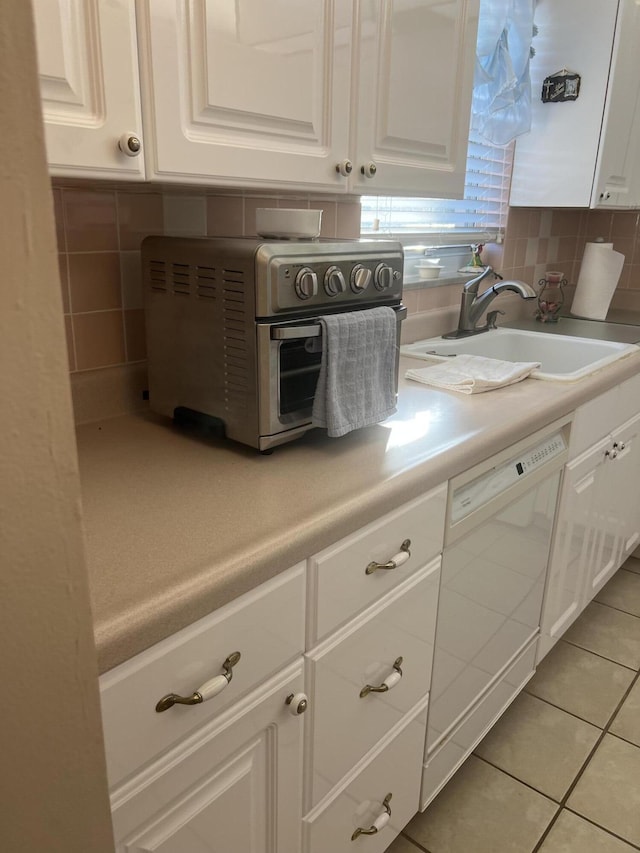 kitchen with light tile patterned floors, sink, backsplash, dishwasher, and white cabinets