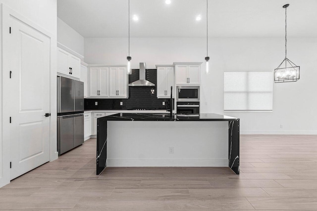 kitchen featuring wall chimney range hood, hanging light fixtures, white cabinets, and appliances with stainless steel finishes