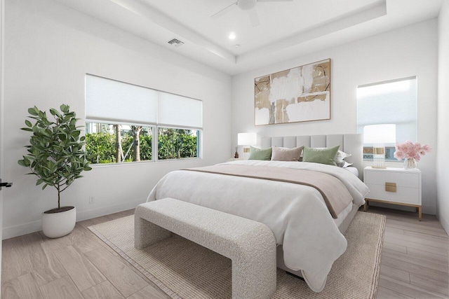 bedroom with a raised ceiling, ceiling fan, and light wood-type flooring