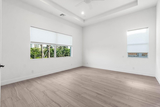 empty room with a tray ceiling, ceiling fan, and light wood-type flooring