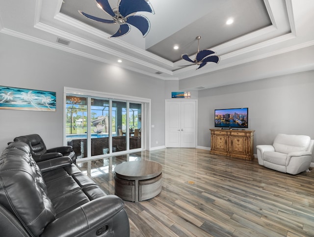 living room with wood-type flooring, ornamental molding, ceiling fan, and a tray ceiling