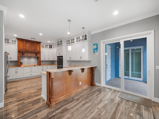 kitchen featuring pendant lighting, stainless steel refrigerator, white cabinetry, a kitchen bar, and kitchen peninsula