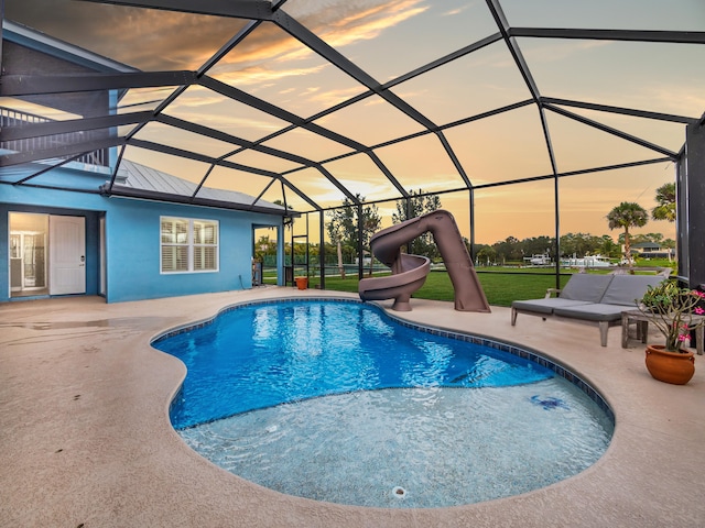 pool at dusk featuring a lanai, a patio area, and a water slide