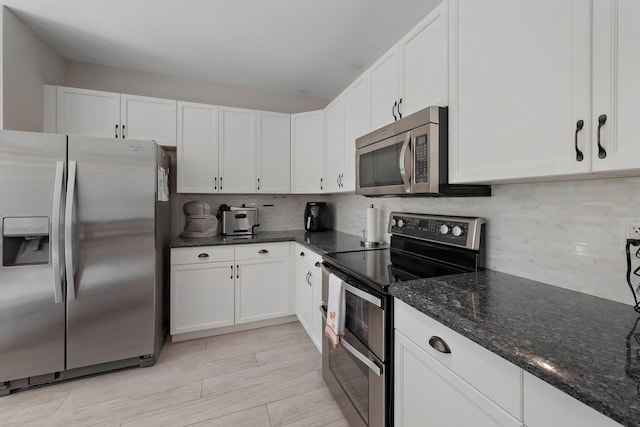 kitchen with dark stone countertops, white cabinets, backsplash, light hardwood / wood-style floors, and stainless steel appliances