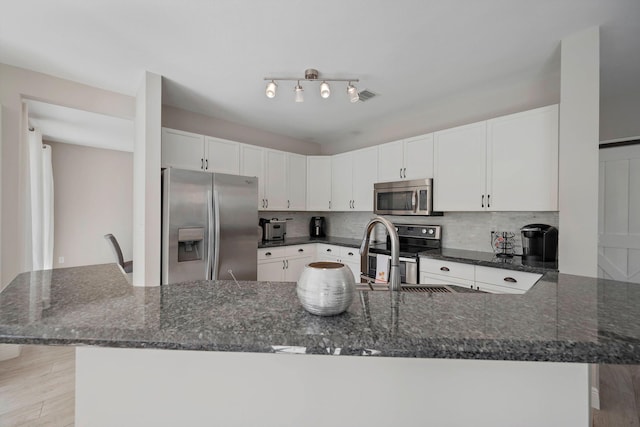 kitchen featuring a breakfast bar area, white cabinetry, dark stone countertops, stainless steel appliances, and backsplash