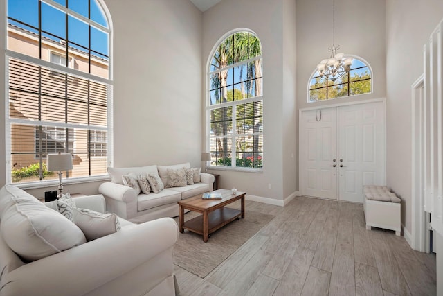 living room with a high ceiling, plenty of natural light, a chandelier, and light hardwood / wood-style flooring