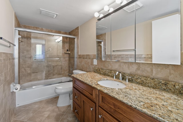 full bathroom featuring combined bath / shower with glass door, tile walls, vanity, tile patterned floors, and toilet