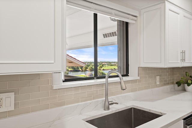 kitchen featuring light stone countertops, sink, decorative backsplash, and white cabinets