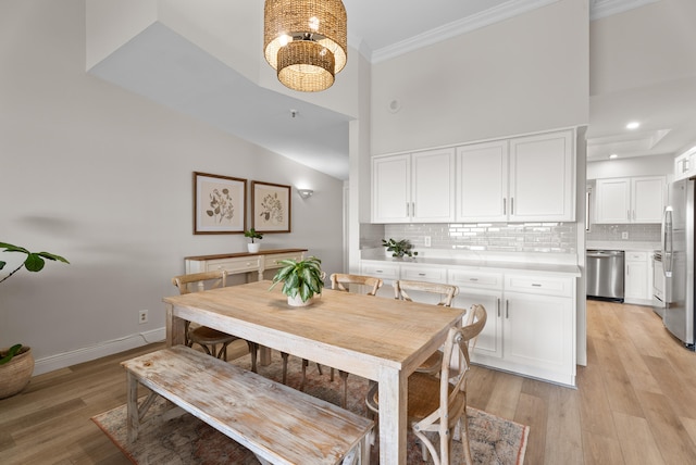 dining room featuring a towering ceiling, ornamental molding, a notable chandelier, and light wood-type flooring