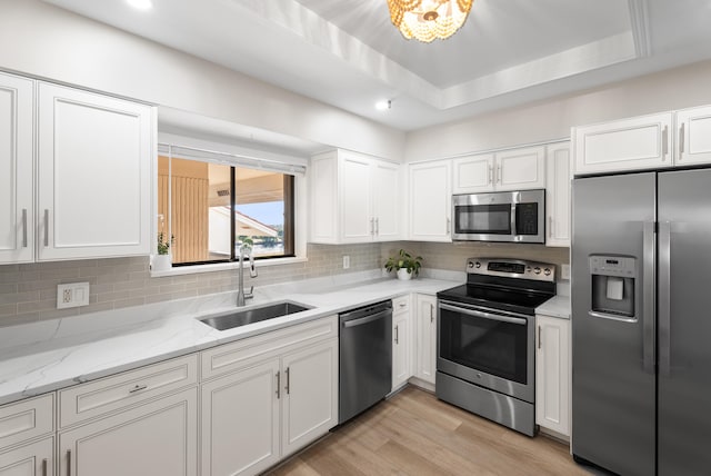 kitchen featuring stainless steel appliances, sink, white cabinets, and a tray ceiling