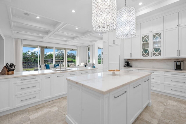 kitchen with a kitchen island, decorative light fixtures, white cabinetry, sink, and coffered ceiling