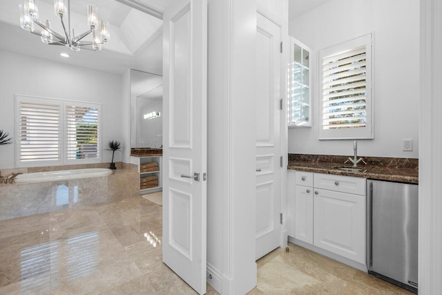 bathroom featuring tiled tub, vanity, and an inviting chandelier