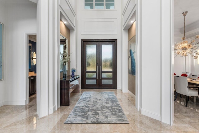 entryway featuring french doors, a towering ceiling, and a chandelier