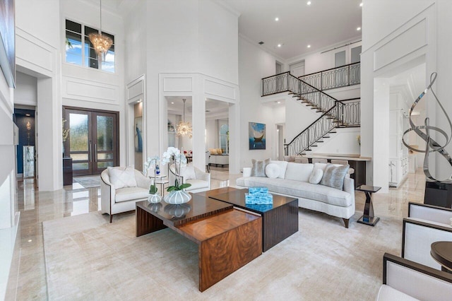 living room with french doors, a towering ceiling, crown molding, and a notable chandelier