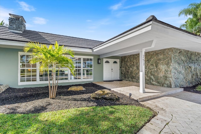 entrance to property featuring a tiled roof, a chimney, and stucco siding