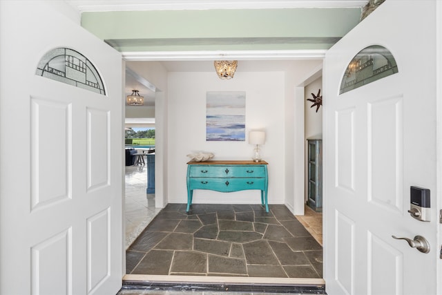 entrance foyer featuring baseboards, stone finish floor, and an inviting chandelier