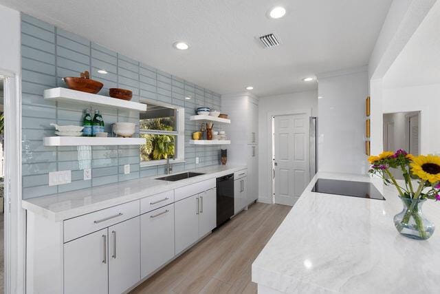 kitchen featuring sink, white cabinetry, light stone counters, black appliances, and decorative backsplash