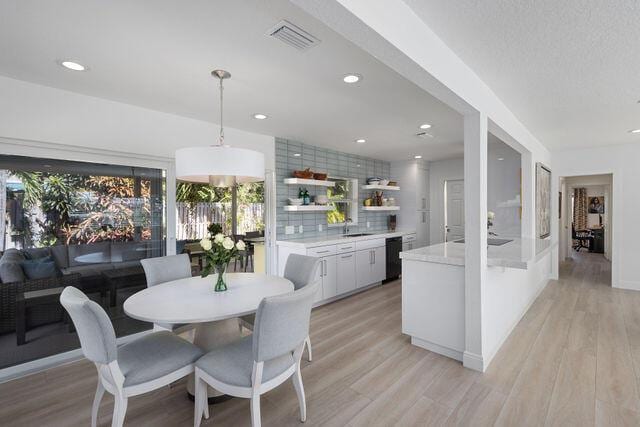 kitchen with white cabinetry, tasteful backsplash, decorative light fixtures, and light hardwood / wood-style flooring