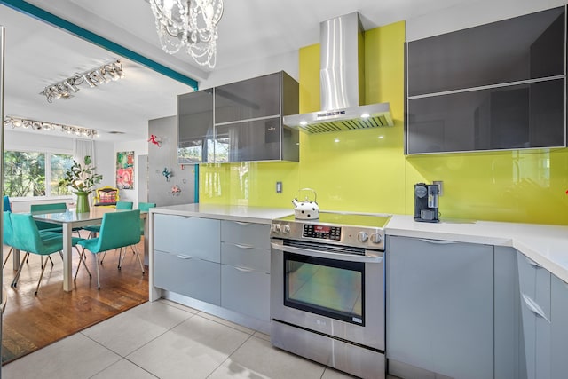 kitchen with rail lighting, a chandelier, light tile patterned floors, wall chimney range hood, and electric stove