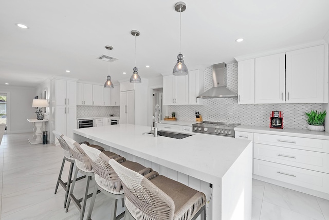 kitchen with white cabinetry, sink, stove, a kitchen island with sink, and wall chimney range hood