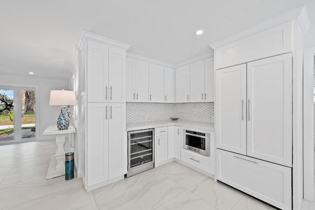 kitchen featuring wine cooler, white cabinetry, crown molding, stainless steel oven, and backsplash