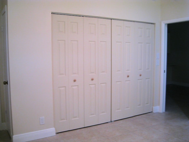 unfurnished bedroom with light tile patterned floors, a closet, and baseboards