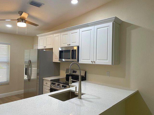kitchen with stainless steel appliances, light countertops, a ceiling fan, white cabinets, and vaulted ceiling