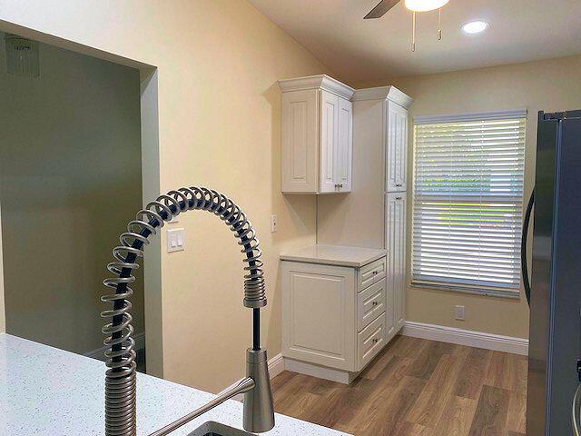 interior space featuring freestanding refrigerator, white cabinetry, dark wood-style flooring, light countertops, and a ceiling fan