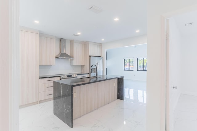 kitchen featuring light brown cabinetry, sink, appliances with stainless steel finishes, a kitchen island with sink, and wall chimney range hood